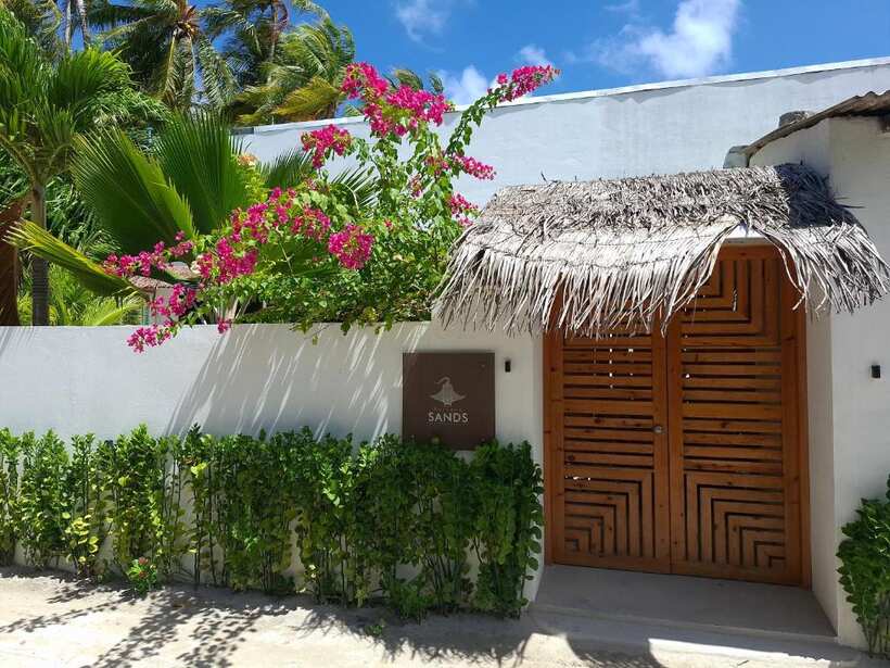 Entrance of Futtaru Sands guesthouse in Gaafaru with bougainvillea and palm trees